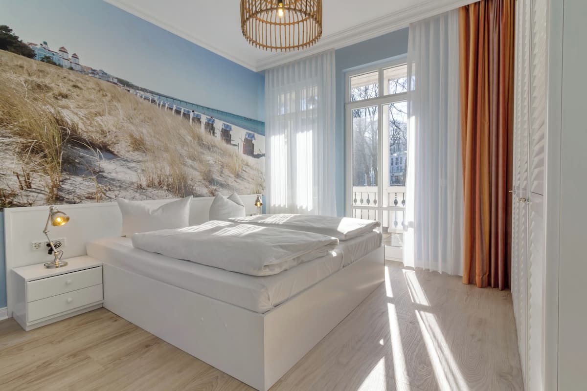 Un dormitorio con cama, mesita de noche, lámpara y un mural en la pared.