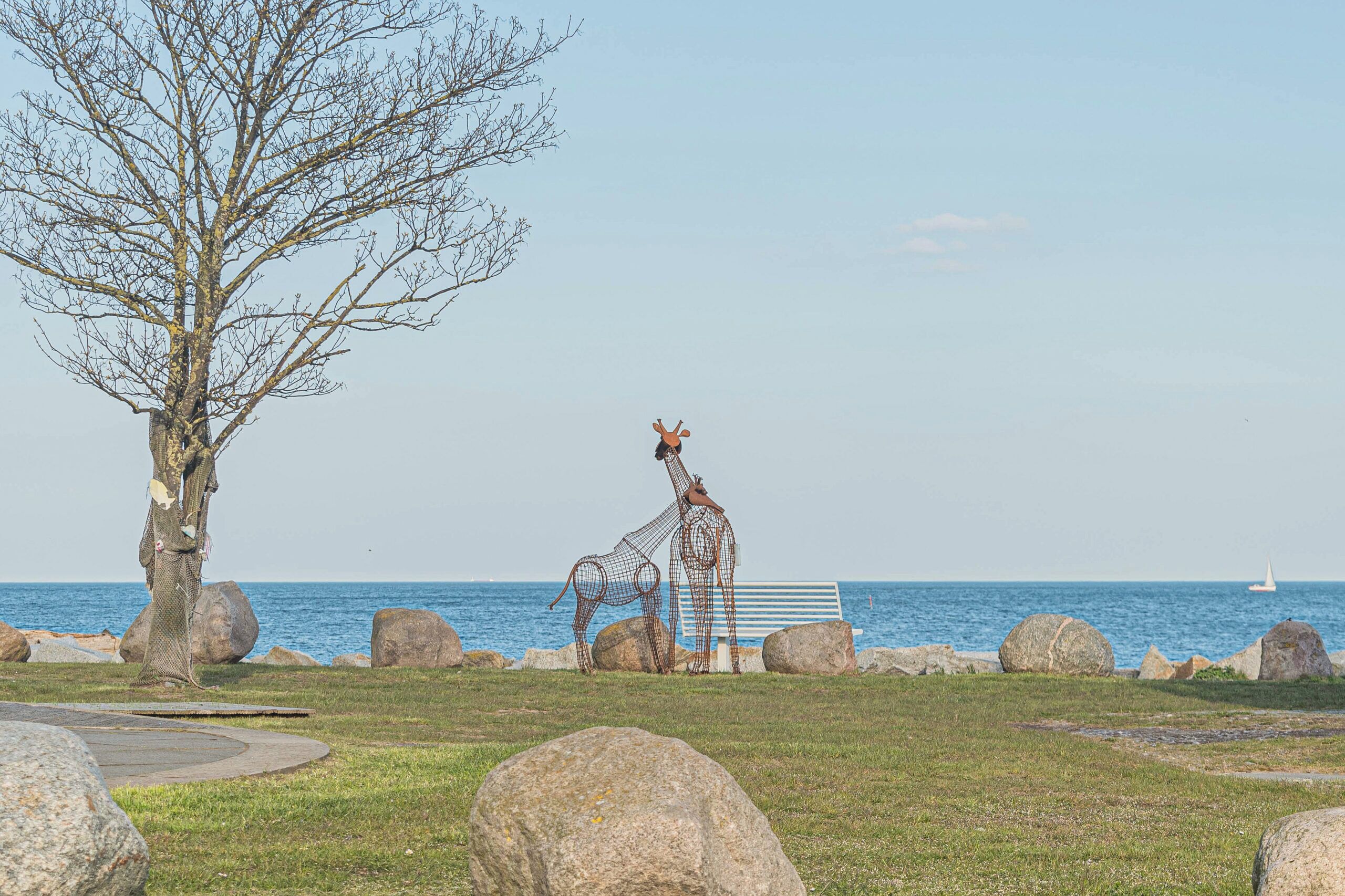 Eine Skulptur von Giraffen in der Nähe einer Bank am Meer.