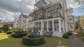 Un edificio grande de varios pisos con un estilo arquitectónico clásico, con múltiples balcones y un jardín bien cuidado.