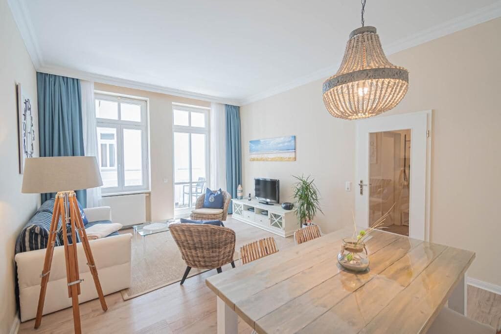 En moderne stue med spiseplads, et fjernsyn og et stort vindue med gardiner.