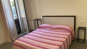 A bedroom with a bed, a window with curtains, a radiator, and a small table. - Newly renovated house, bright and within walking distance of Ortigia and the Greek theater. (Siracusa)