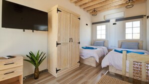 Een slaapkamer met twee bedden, een televisie, een houten garderobe en een plant.
