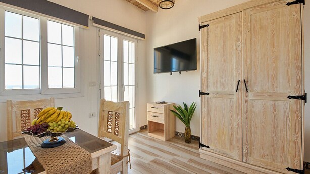 Een kamer met houten vloer, een tafel met een fruitschaal, een stoel, een televisie aan de muur en een grote houten garderobe.