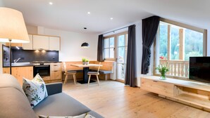 A modern living room with a sofa, a dining table with chairs, a kitchen area, and a TV on a wooden stand. - Apartment 'Altmessnerhof Alpenklee' with Mountain View, Shared Terrace and Wi-Fi (Dobbiaco)