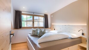 A bedroom with a wooden headboard, a window with curtains, a bedside table, and a bed with pillows. - Apartment 'Altmessnerhof Alpenklee' with Mountain View, Shared Terrace and Wi-Fi (Dobbiaco)