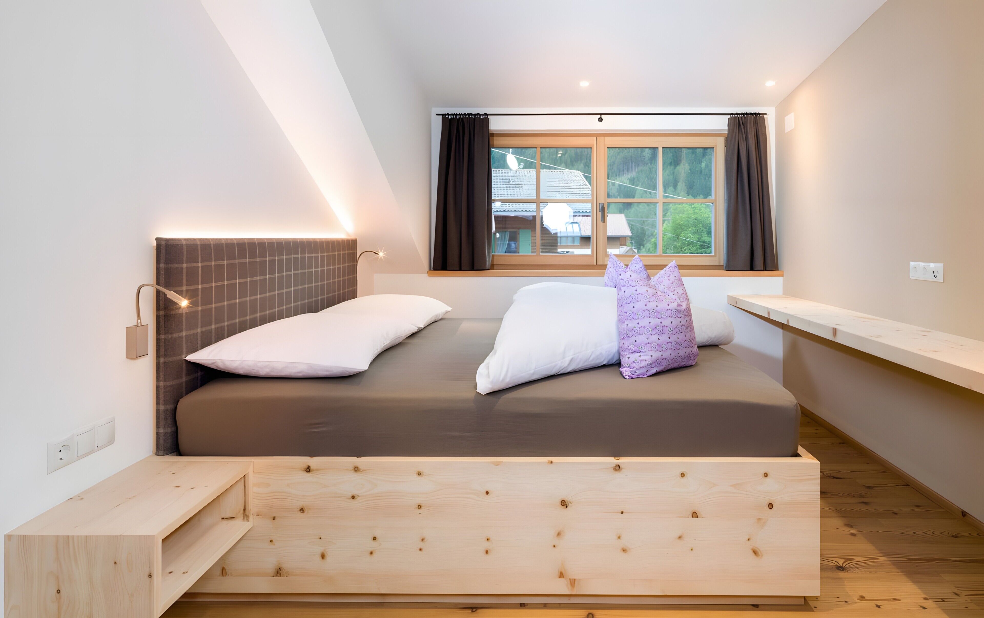 Een moderne slaapkamer met een bed, een raam met gordijnen, een nachtkastje en een wandlamp.