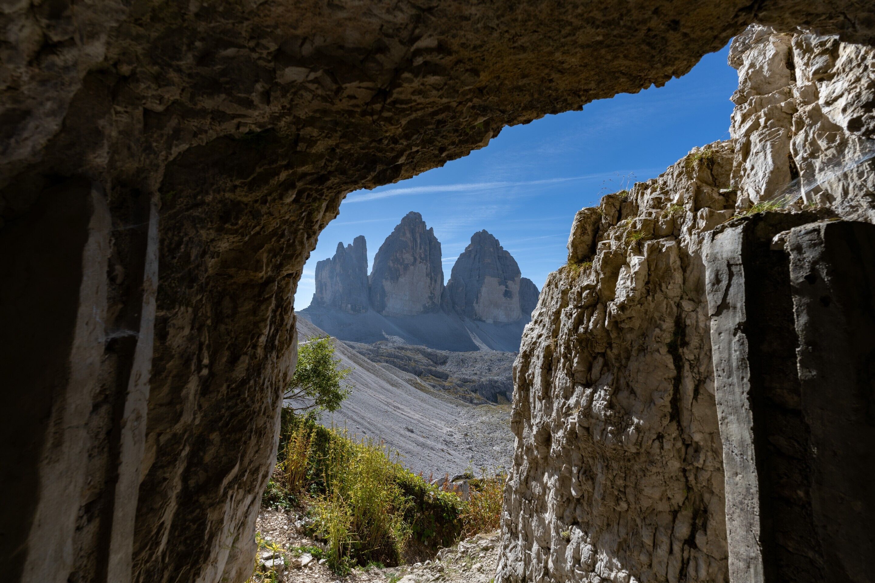 A natural rock formation with a cave entrance, rugged terrain, and distant mountain peaks.
