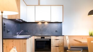 A modern kitchen with wooden cabinets, a built-in oven, and a dining area with a wooden table and chairs. - Apartment 'Altmessnerhof Alpenklee' with Mountain View, Shared Terrace and Wi-Fi (Dobbiaco)
