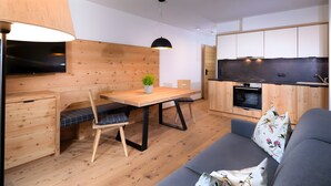 A modern kitchen with wooden cabinetry, a dining table with chairs, a sofa, and a TV. - Apartment 'Altmessnerhof Glücksklee' with Mountain View, Shared Terrace and Wi-Fi (Dobbiaco)