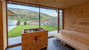 Ein Holzinnenraum mit Sauna, einer hölzernen Bank und Blick auf eine Berglandschaft.