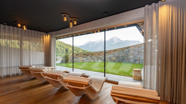 A room with wooden flooring, a large window with a mountain view, and a seating area with cushioned chairs. - Apartment 'Altmessnerhof Steinklee' with Mountain View, Shared Terrace and Wi-Fi (Dobbiaco)