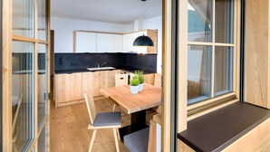 A modern kitchen with wooden cabinetry, a black countertop, and a dining area with a wooden table and chairs. - Apartment 'Altmessnerhof Steinklee' with Mountain View, Shared Terrace and Wi-Fi (Dobbiaco)