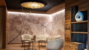 A room with wooden flooring, a chandelier, a wall with leaf patterns, and a wooden shelf with decorative items. - Apartment 'Altmessnerhof Steinklee' with Mountain View, Shared Terrace and Wi-Fi (Dobbiaco)