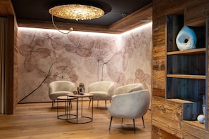 Une pièce dotée d’un parquet en bois, d’un lustre, d’un mur orné de motifs végétaux et d’une étagère en bois sur laquelle sont disposés des objets décoratifs.