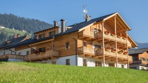 A wooden chalet with multiple balconies, a sloped roof, and a view of a forested hillside.