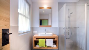 A modern bathroom with a wooden vanity, a glass shower enclosure, and a window with curtains.