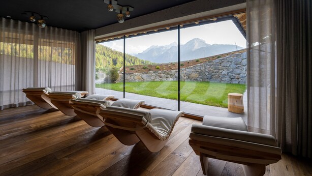 A room with wooden massage chairs, a large window with a mountain view, and a stone wall.