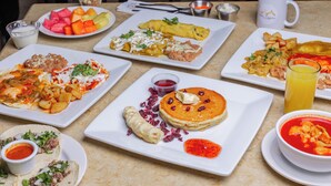 Ein Tisch mit verschiedenen Frühstücksgerichten, darunter Pfannkuchen, Omeletts und Tacos.