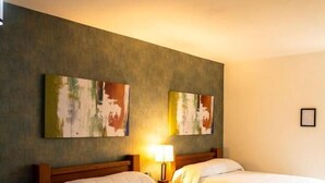 Ein Hotelzimmer mit zwei Betten, einem Nachttisch mit Lampe und zwei abstrakten Bildern an der Wand.