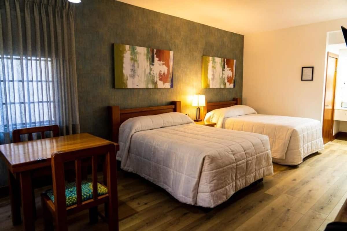 Habitación de hotel con dos camas, un escritorio de madera, una silla y obras de arte en la pared.