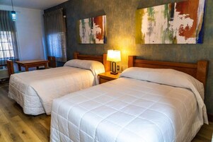 Habitación de hotel con dos camas, una mesa y una lámpara.