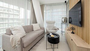 Een moderne woonkamer met een bank, fauteuil, een rond bijzettafeltje en een televisie die aan een houten wand is bevestigd.