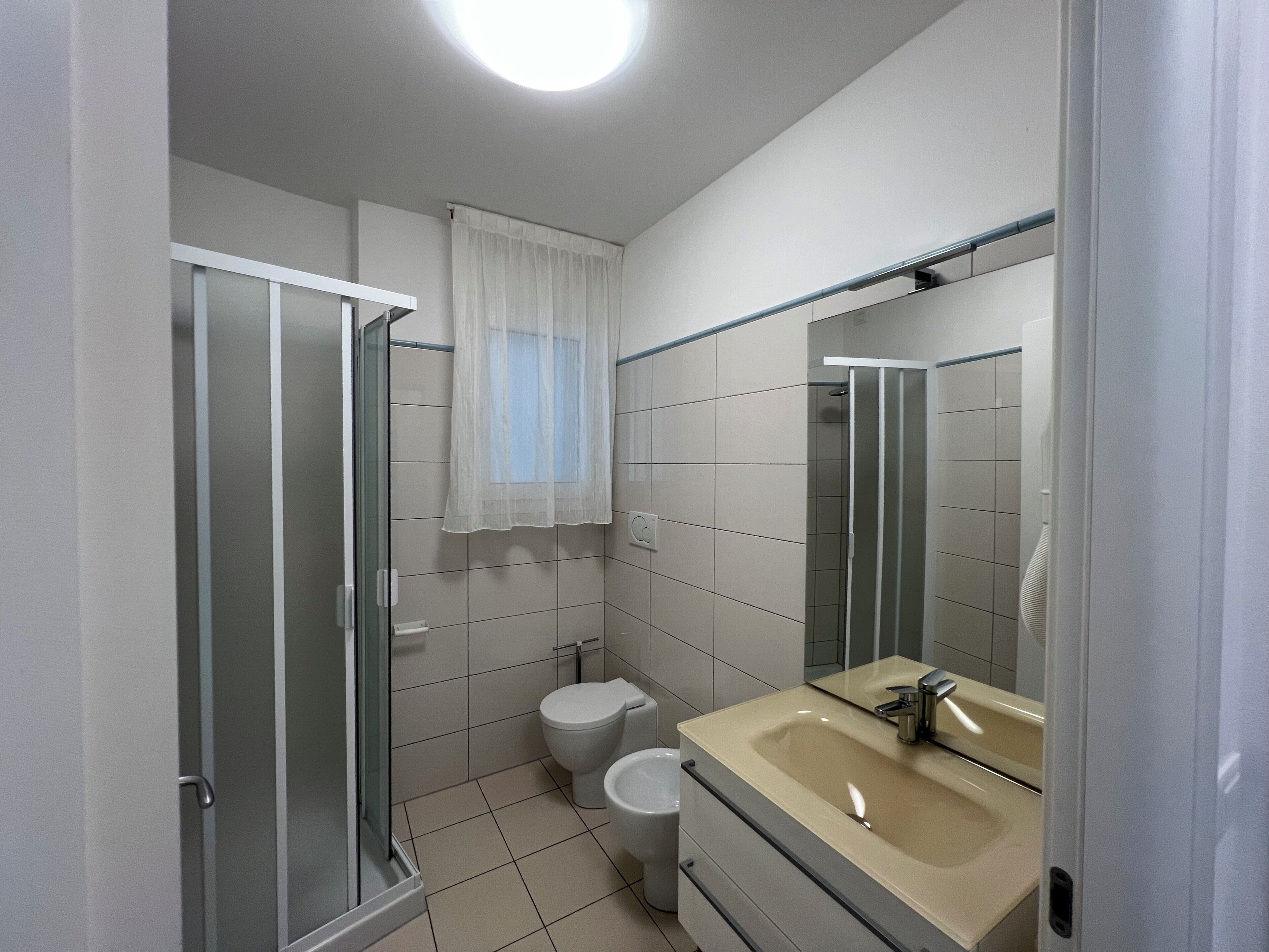 A bathroom with a glass shower enclosure, a toilet, and a sink with a mirror.