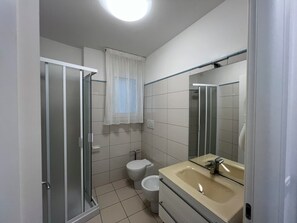 A bathroom with a glass shower enclosure, a toilet, and a sink with a mirror. - Modern Flat 50mt From the Beach (Lignano Sabbiadoro)
