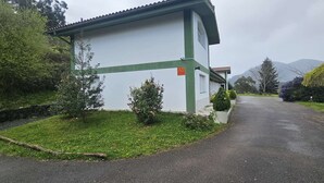 A white building with a green trim, a paved driveway, and a mountain in the background.