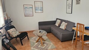 A living room with a grey sofa, a glass coffee table, a wooden dining table, and a black chair.