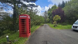 A red telephone booth on a rural road with a van parked nearby.