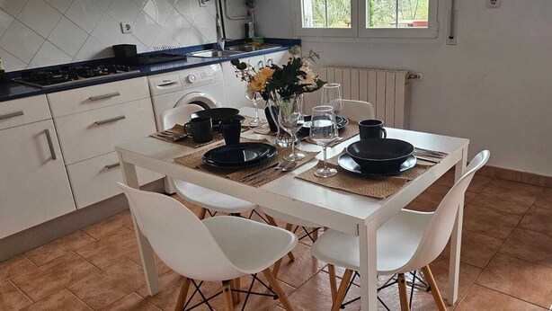 A kitchen with white cabinets, a black countertop, and a dining table set with plates, cups, and a vase with flowers.