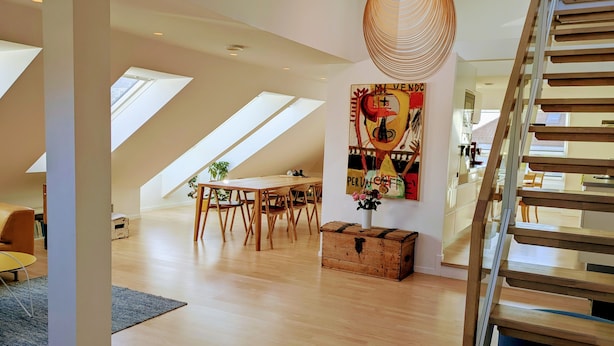 Ein geräumiges Loft mit hohen Decken, Dachfenstern, einem Holzessttisch und einer Treppe.