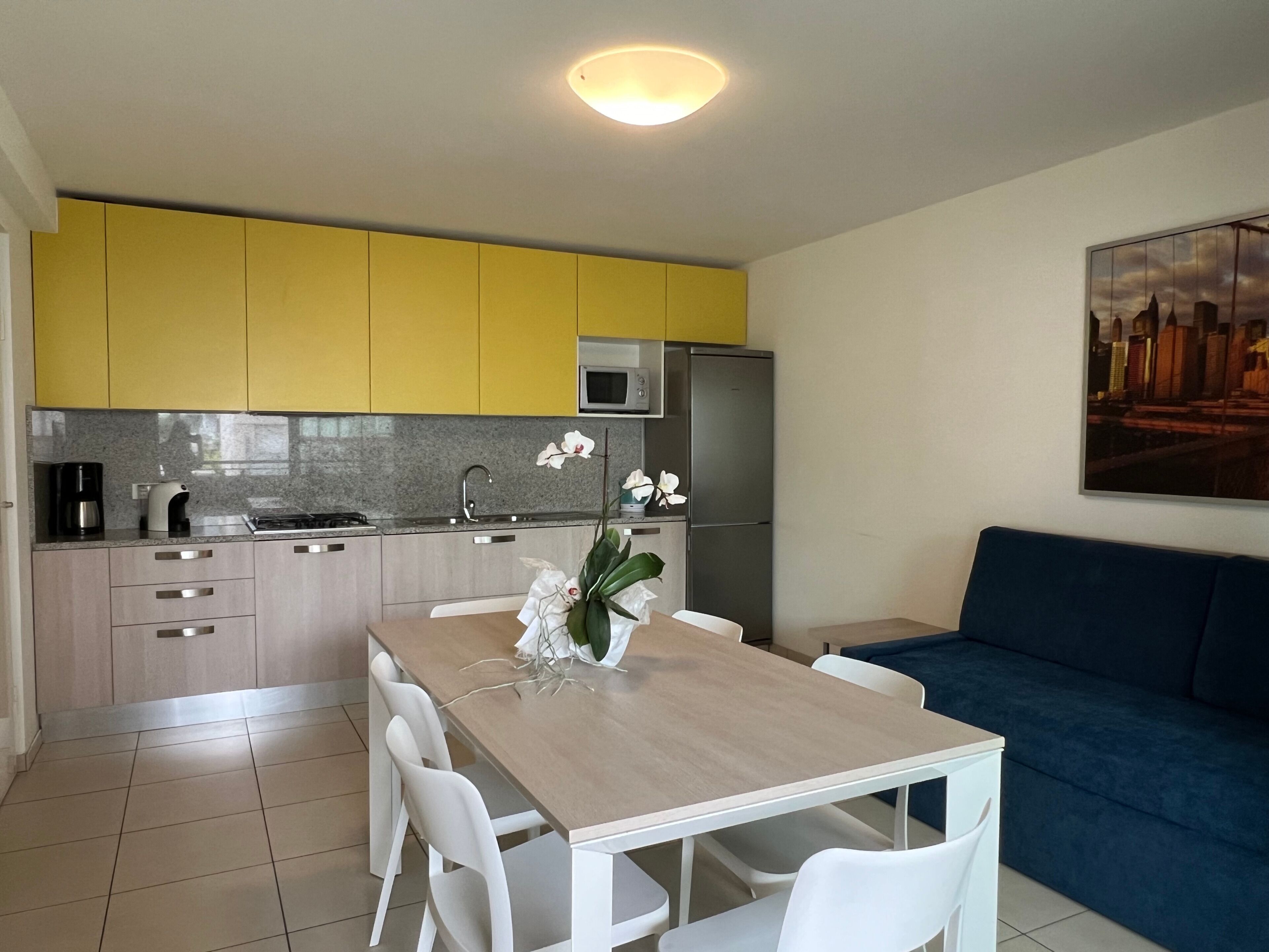 Eine moderne Küche mit gelben Schränken, einem Edelstahl-Kühlschrank und einem Esstisch mit weißen Stühlen.