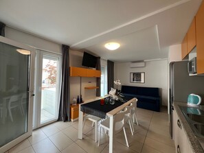 A modern kitchen with a dining area, a built-in microwave, and a sliding glass door leading to a balcony. - Seaside Flat With Spacious Balcony (Lignano Sabbiadoro)