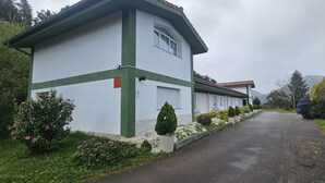 Ein Gebäude mit weißer Fassade und grünen Verzierungen, einer gepflasterten Auffahrt und einem Garten mit verschiedenen Pflanzen.