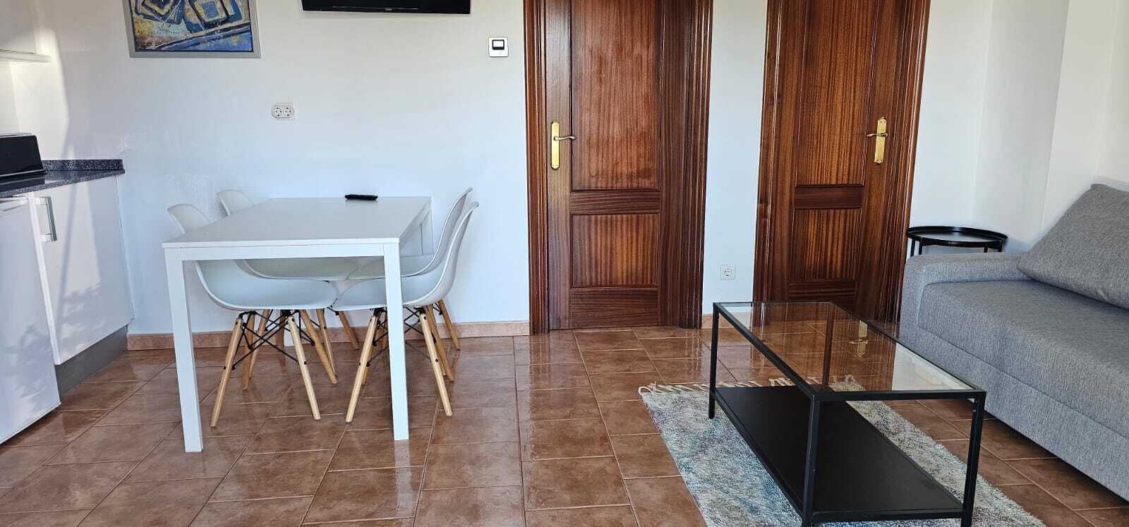 Una sala de estar con un sofá, una mesa de comedor con sillas, una mesa de centro y una zona de cocina con mostrador y armarios.