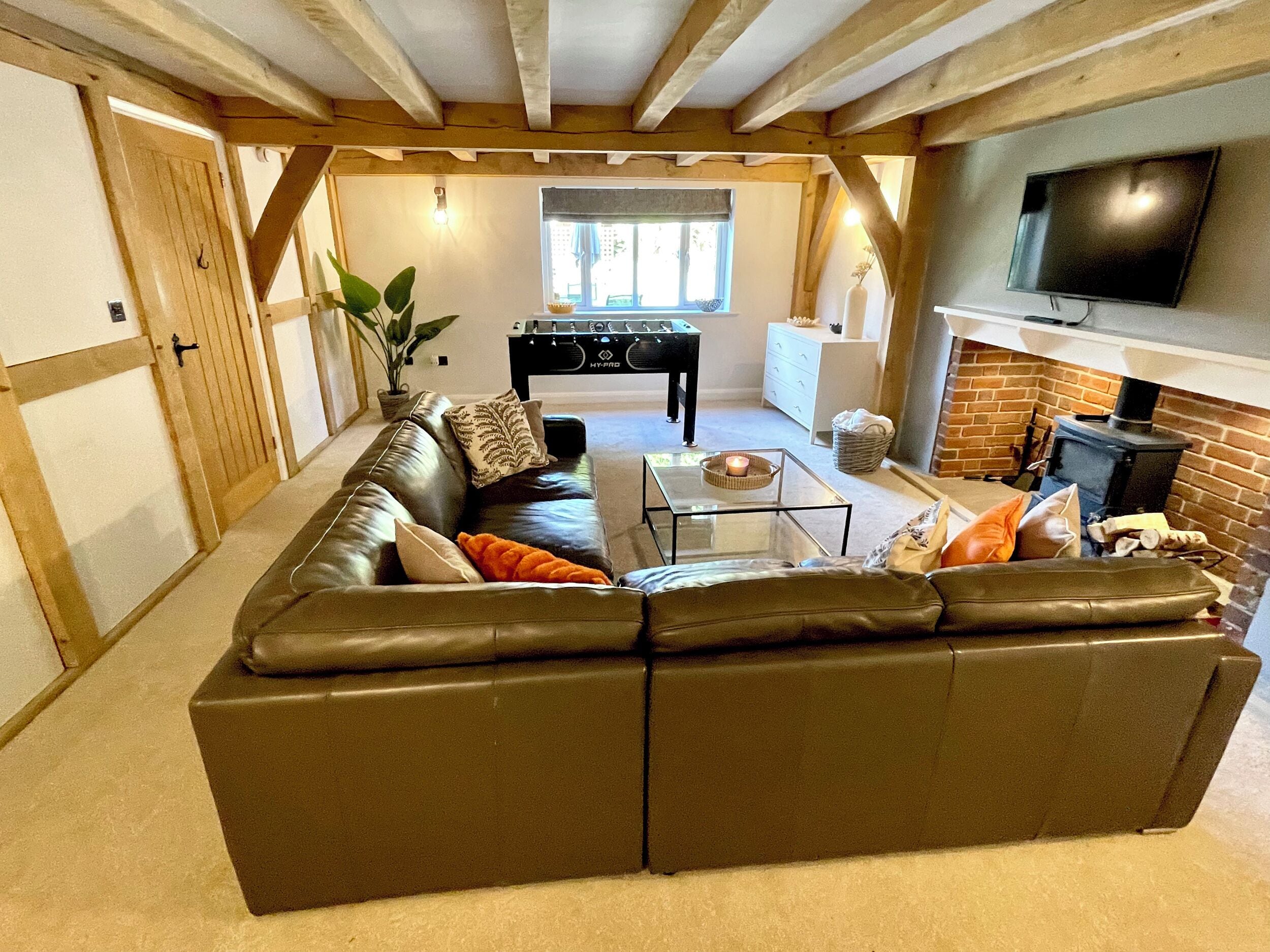 A cozy living room with a leather sofa, a glass coffee table, a fireplace, and a television mounted on the wall.