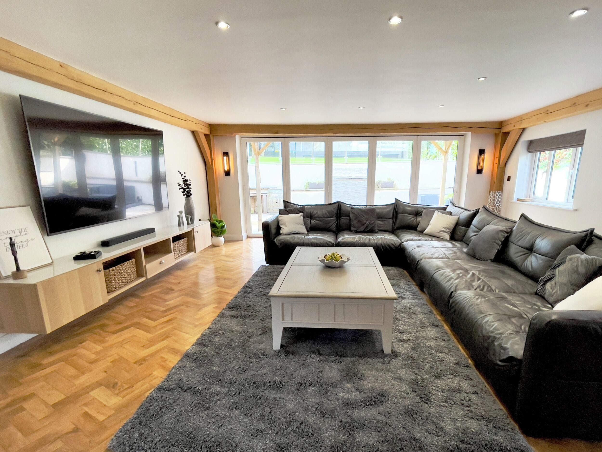 A modern living room with a large flat-screen TV, a leather sofa, a white coffee table, and a wooden floor.