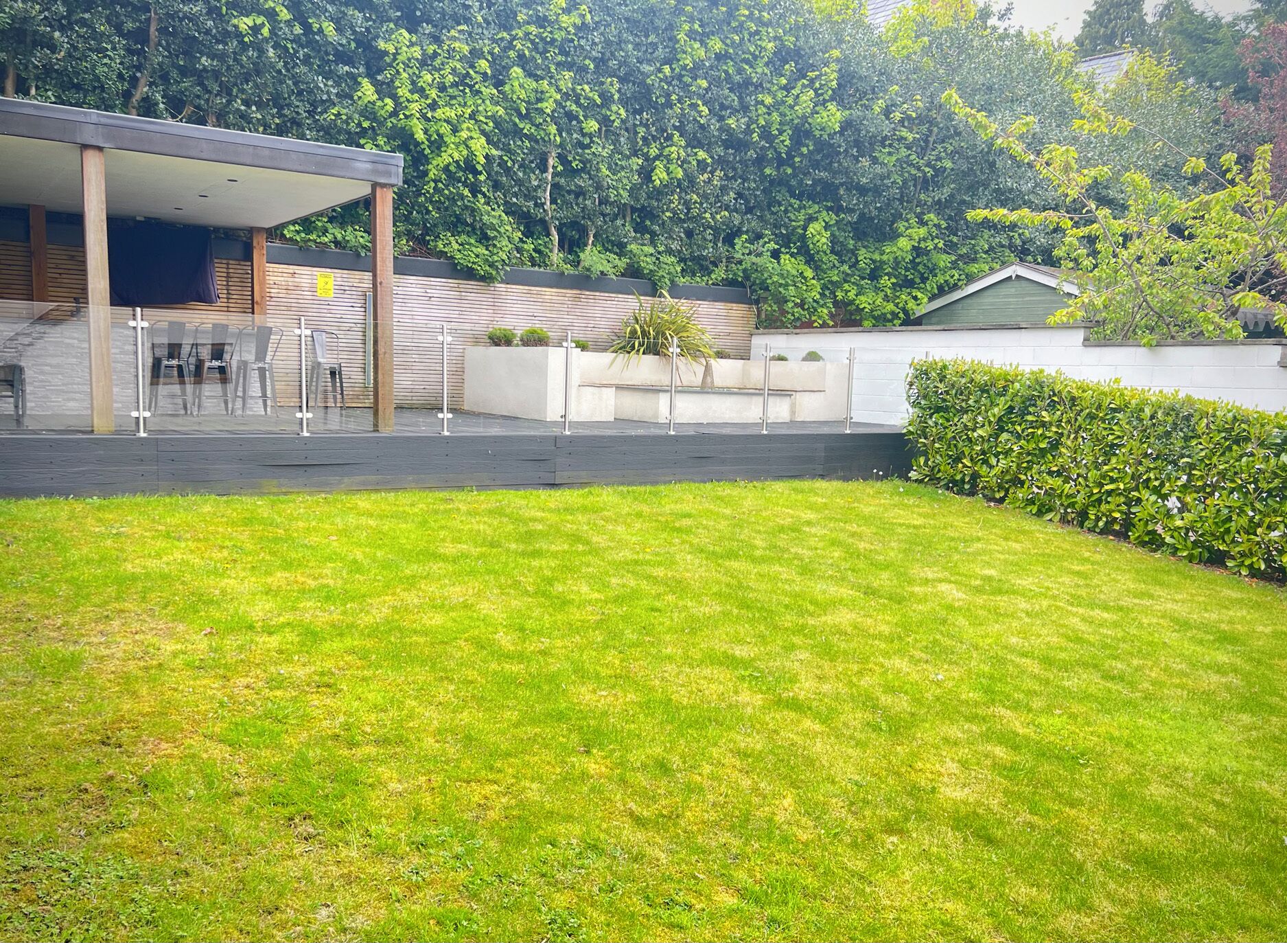 A modern building with a covered outdoor seating area, a well-maintained lawn, and a hedge.