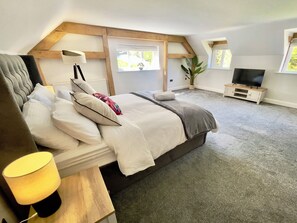 A bedroom with a bed, bedside lamp, TV, windows, and a plant. - The Oaks (Blackburn)