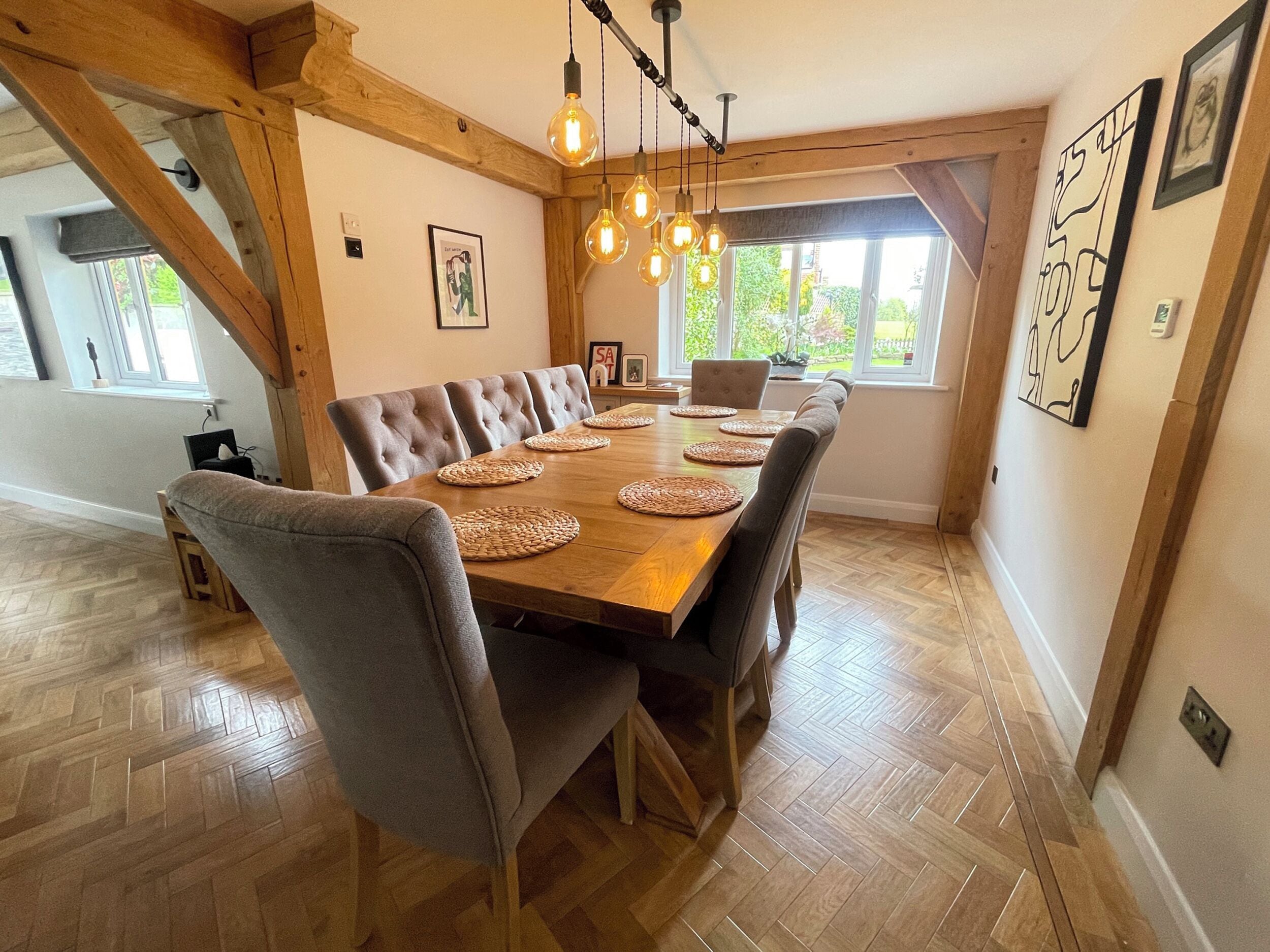 Un comedor con mesa de madera, sillas tapizadas en gris, individuales tejidos e iluminación colgante.