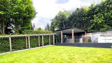 A covered outdoor area with a wooden pergola, a stone wall, and a grassy lawn.