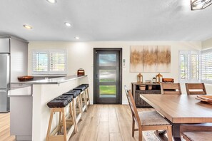 A modern kitchen with a dining area, including a wooden table and bar stools. - Sunset Dreams (St. Pete Beach)