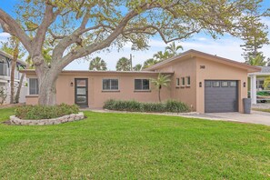 A single-story house with a garage, a well-maintained lawn, and a large tree in the front yard. - Sunset Dreams (St. Pete Beach)