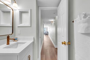 A hallway with a white vanity, a mirror, and a door with a towel hanging on it. - Emerald Isle 501 - Premier (North Redington Beach)