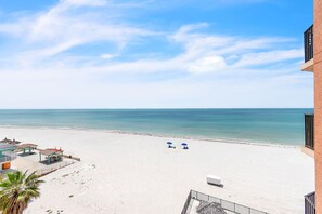 Blick auf einen Strand mit einem Gebäude, zwei Sonnenschirmen und einer Palme.