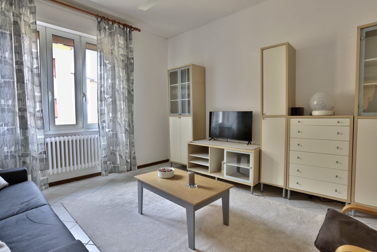 Een woonkamer met een bank, een salontafel, een televisie, een kast en een radiator.