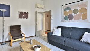 Ein Wohnzimmer mit grauem Sofa, einem Holzstuhl, einem Couchtisch mit Schale und abstrakter Kunst an den Wänden.