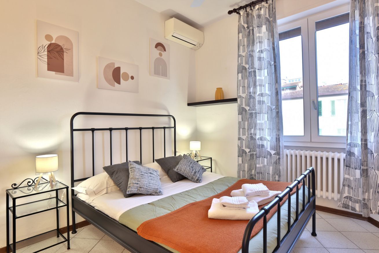 Une chambre à coucher avec un lit, des tables de chevet, une fenêtre avec des rideaux et des œuvres d’art murales.